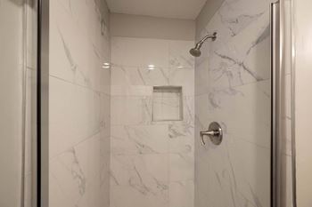 A white marble bathroom with a shower and a door.